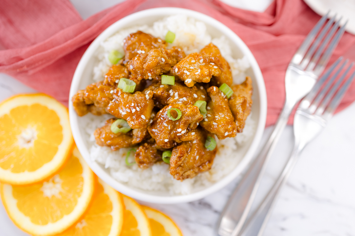 Top view of Orange Chicken on a plate next to slices of orange.