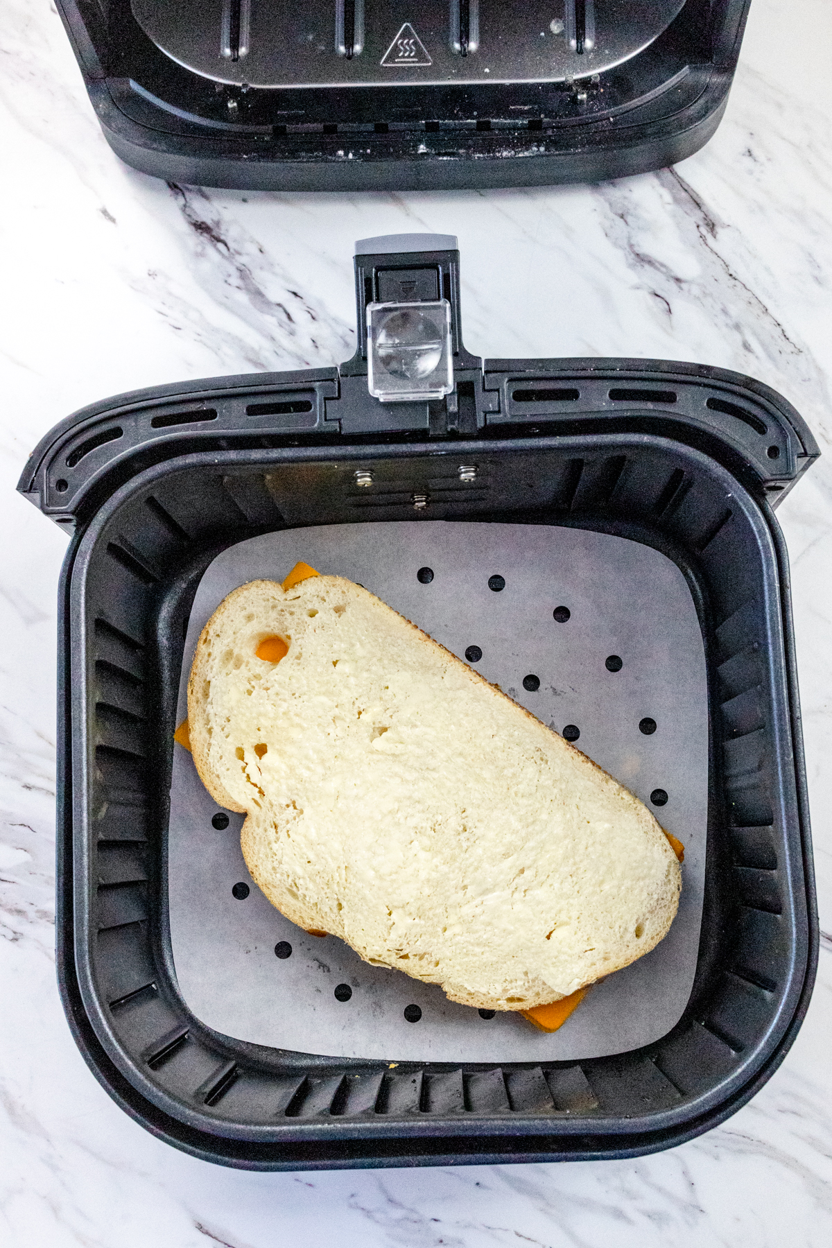 Top view of air fryer basket with a cheese sandwich in it, on top of parchemnet paper.