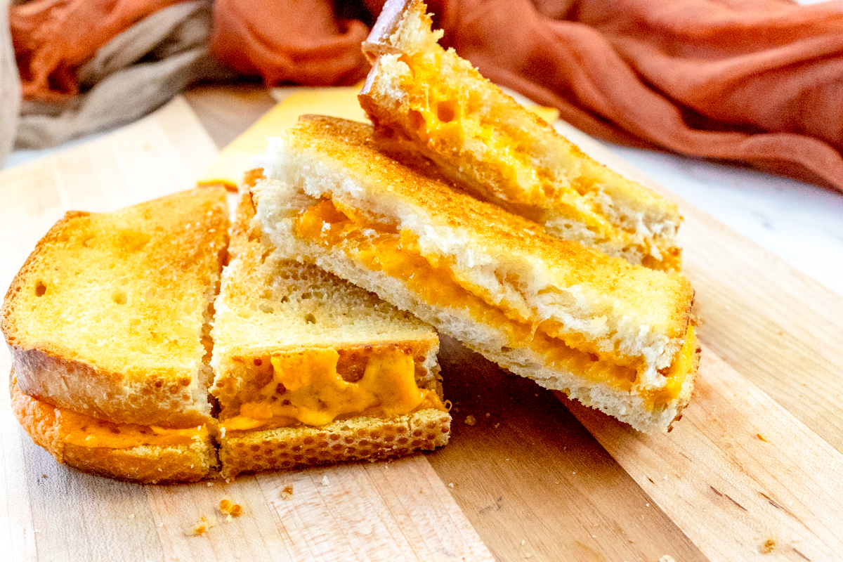 Close-up of an air fryer grilled cheese sandwich sliced on a cutting board.