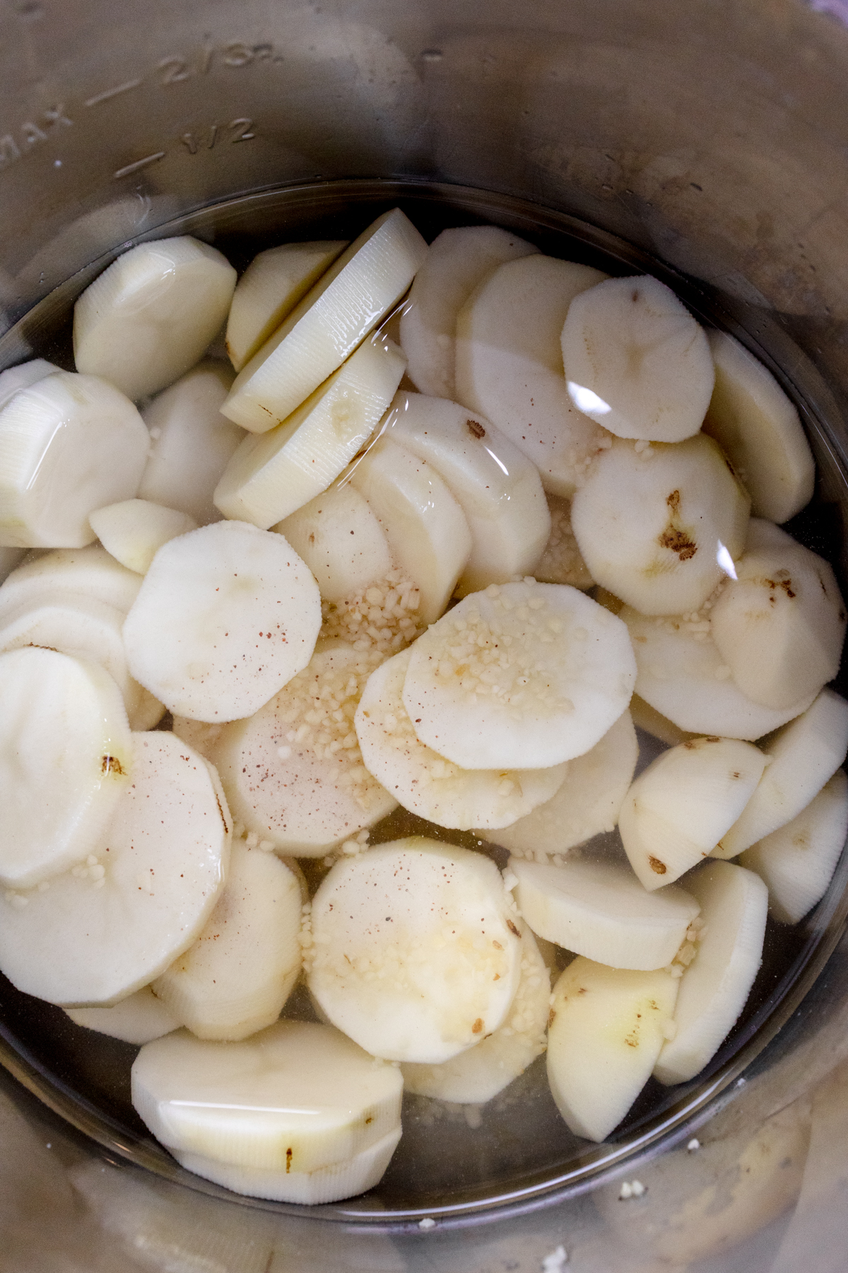 Close-up view of an Instant Pot liner with water, salt, and garlic added to the slices of potato.
