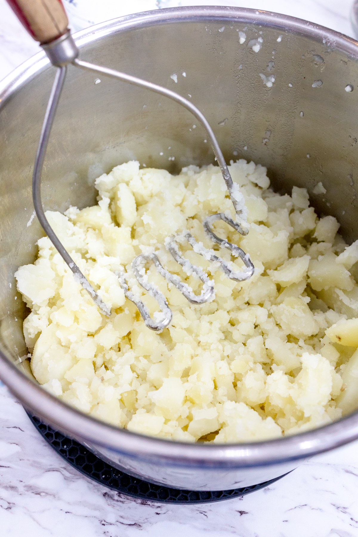 Close up view of a potato masher mashing potatoes in the Instant Pot liner.