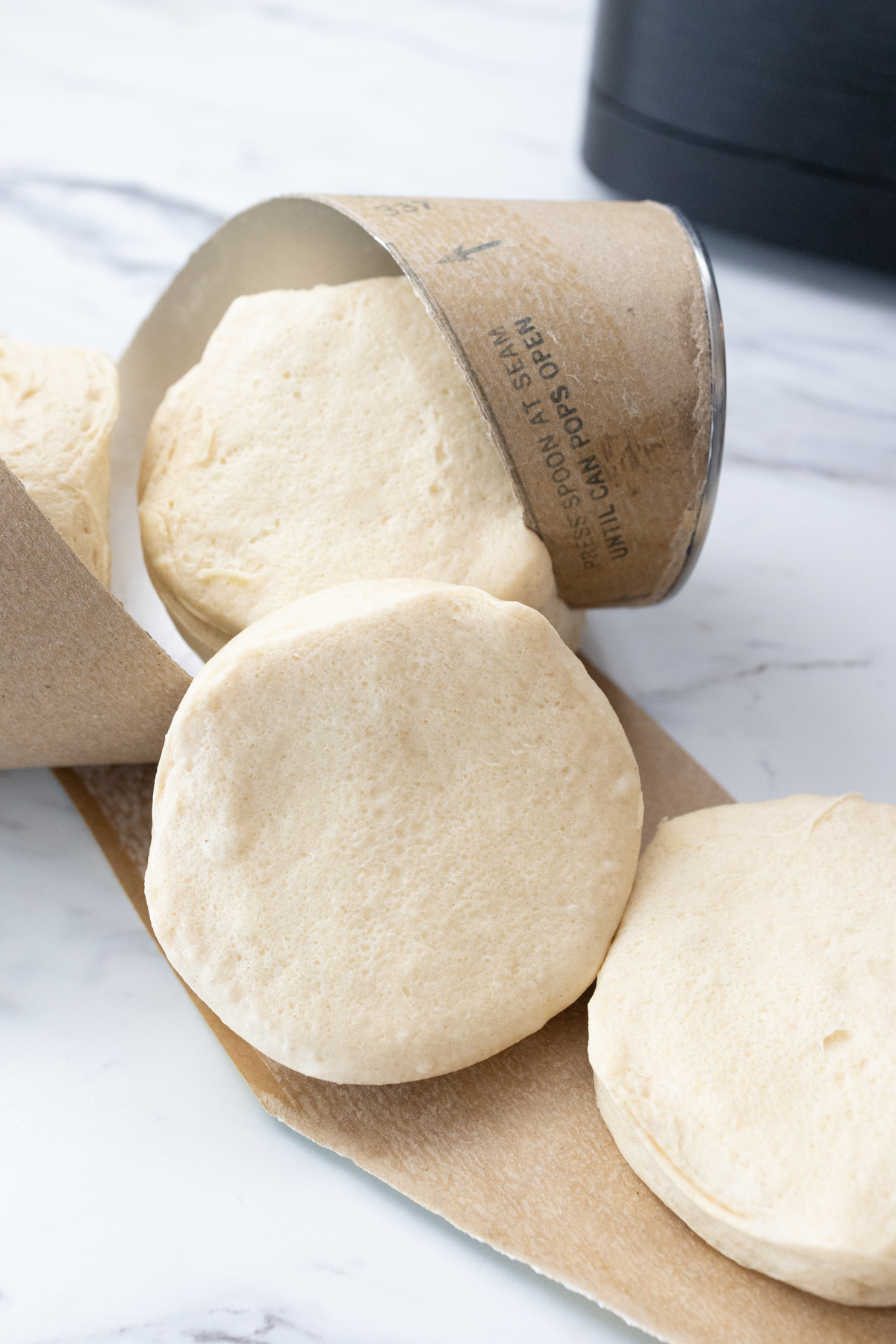 Close up view of biscuits being removed from a can of Pillsbury Grand Biscuits on a white marble surface.