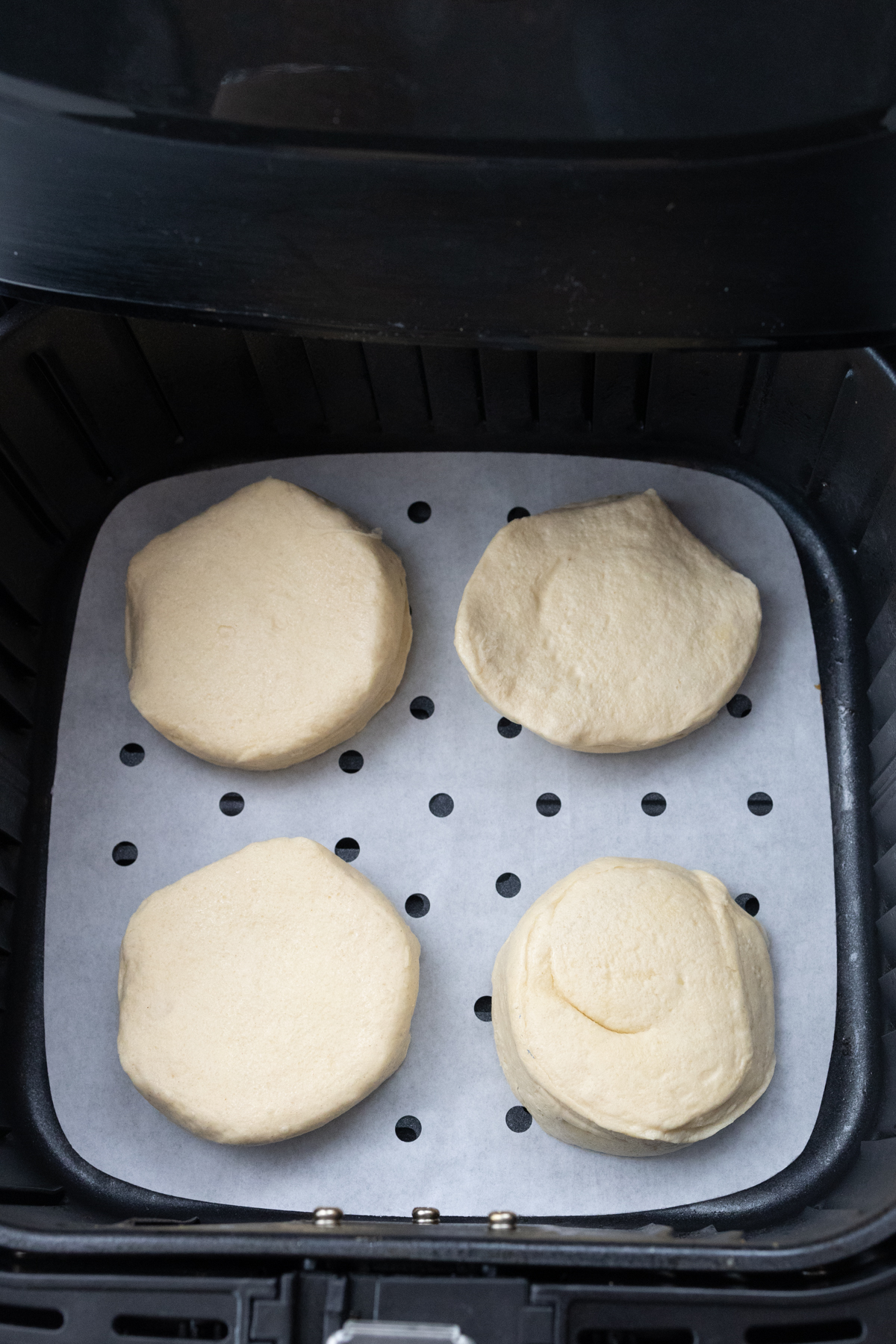 Top view of an open air fryer with four Pillsbury Grand Biscuits in it, ready to cook.