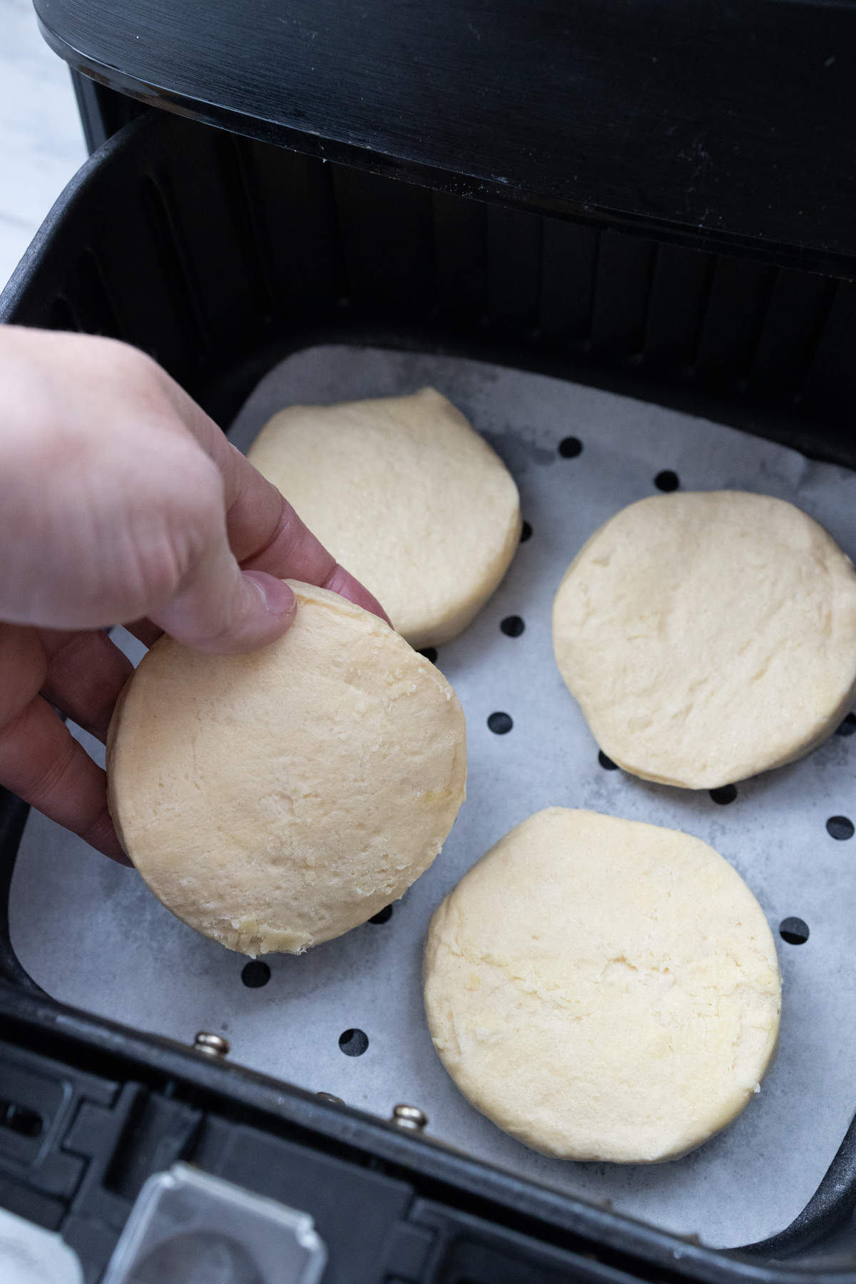 Close up view of a hand placing Pillsbury Grand Biscuits into an open air fryer.