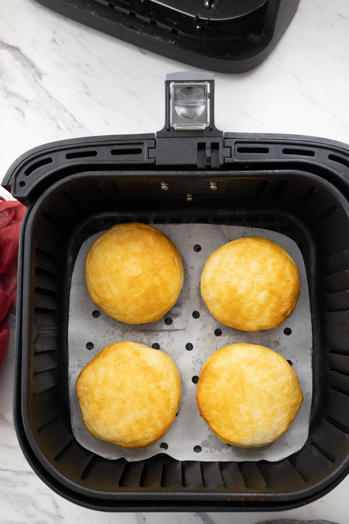 Top view of an open air fryer with four fried Pillsbury Grand Biscuits in it.