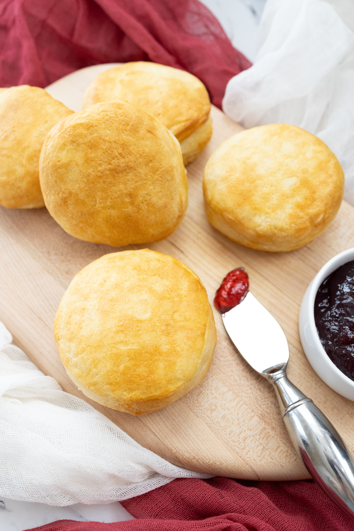 Top view of Pillsbury Grand Biscuits fresh out of the air fryer, on a wooden surface, with a knife next to them that has berry jam on it.