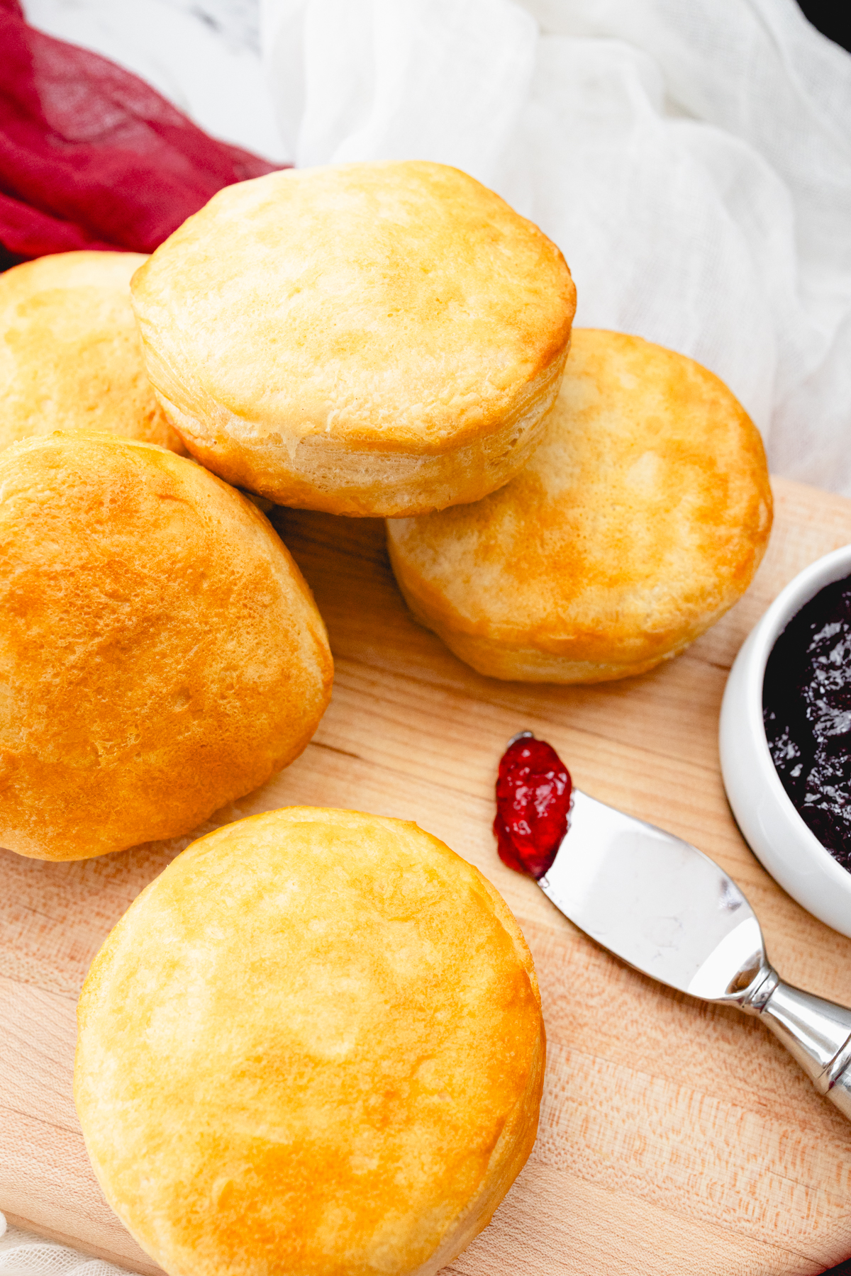 Top view of Pillsbury Grand Biscuits fresh out of the air fryer, on a wooden surface, with a knife next to them that has berry jam on it.