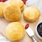 Top view of Pillsbury Grand Biscuits fresh out of the air fryer, on a wooden surface, with a knife next to them that has berry jam on it.