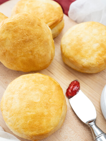 Top view of Pillsbury Grand Biscuits fresh out of the air fryer, on a wooden surface, with a knife next to them that has berry jam on it.