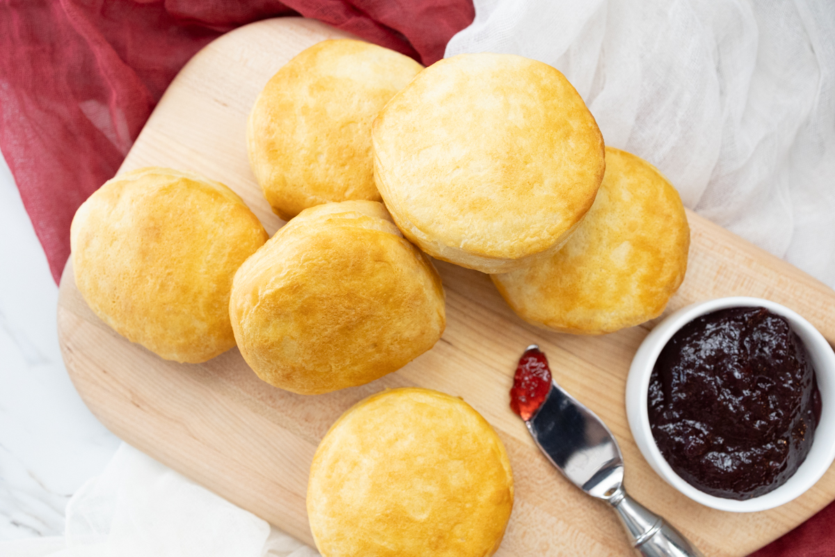 Top view of Pillsbury Grand Biscuits fresh out of the air fryer, on a wooden surface, with a knife next to them that has berry jam on it.