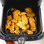 Overhead view of waffle fries in an air fryer.