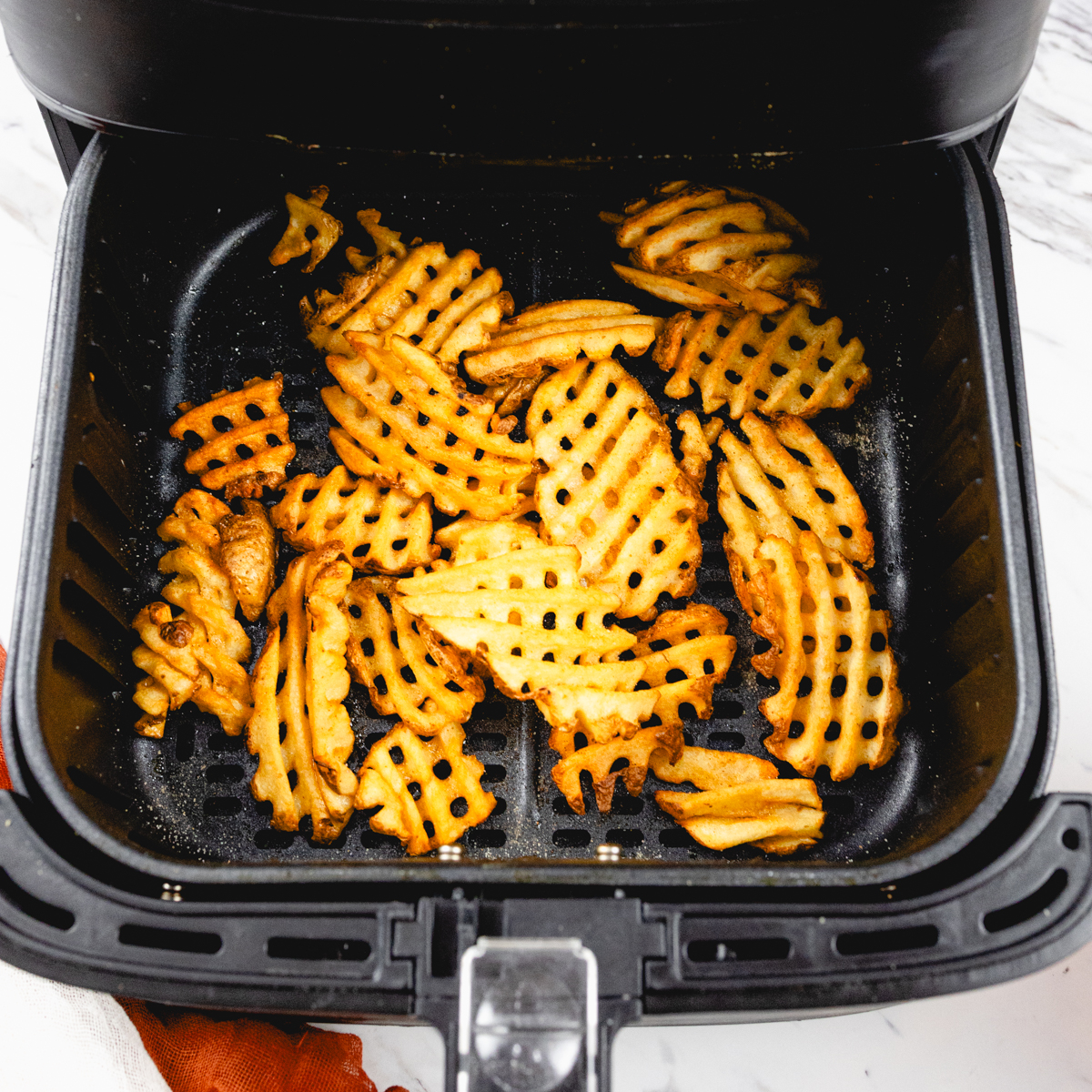 Overhead view of waffle fries in an air fryer.