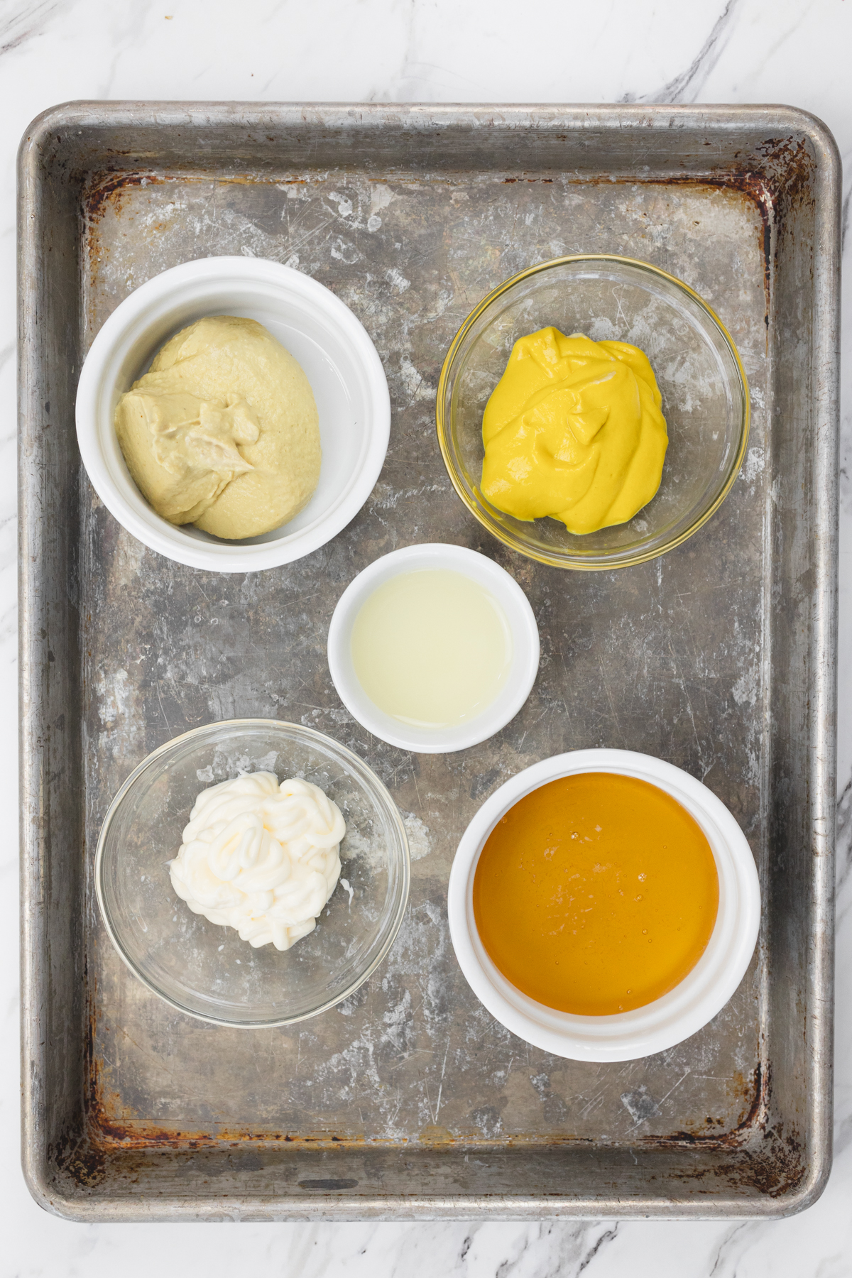 Top view of ingredients needed to make honey mustard dipping sauce in small bowls on a baking tray.