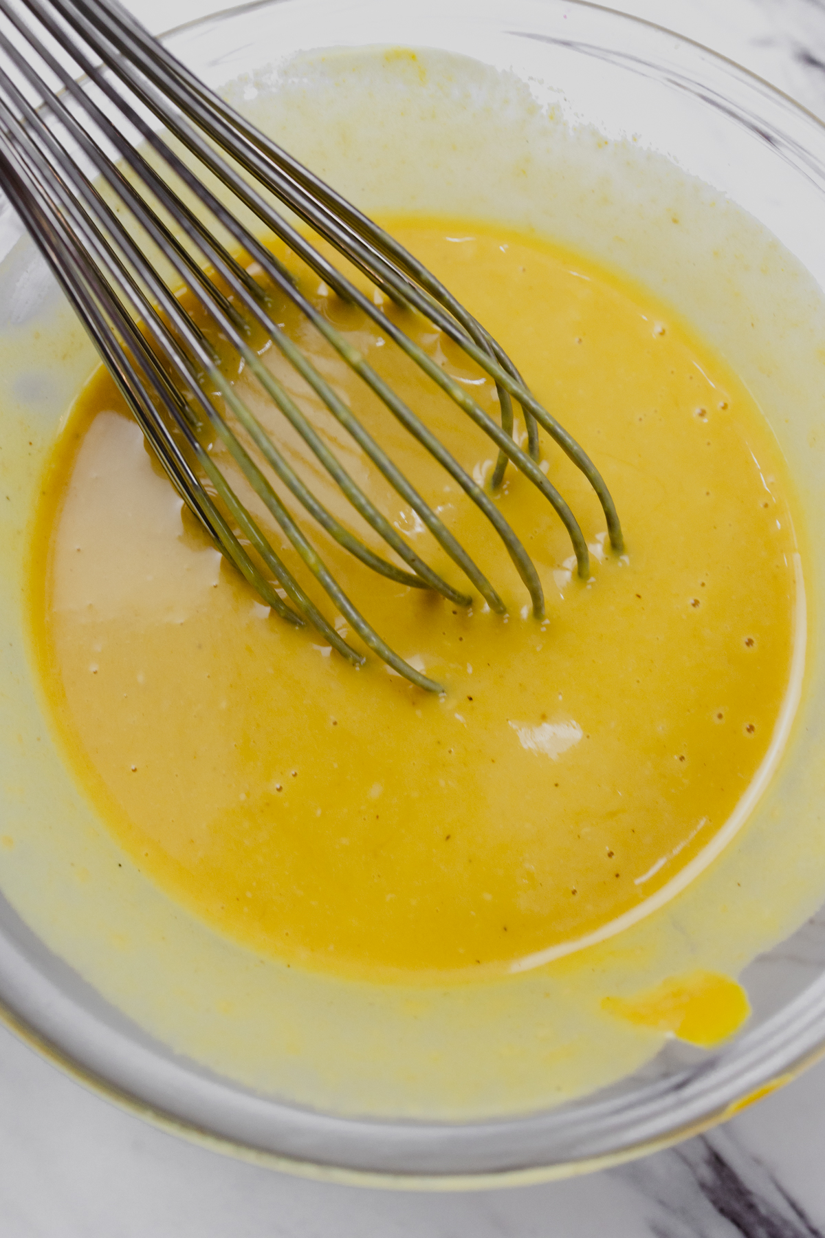 Top view of a small mixing bowl with honey mustard dipping sauce being mixed with a whisk.