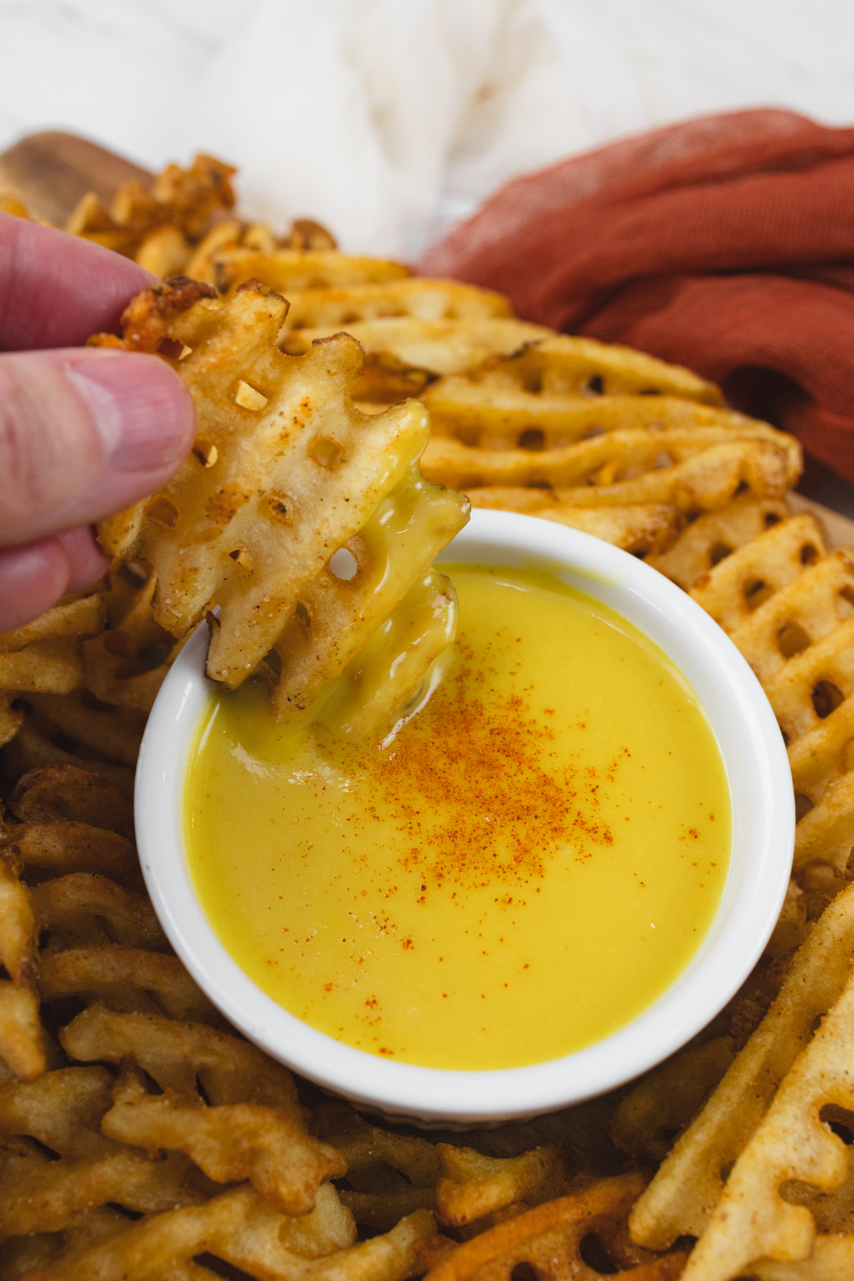 Close up of honey mustard dipping sauce in a ramekin with a waffle fry being dipped into it.