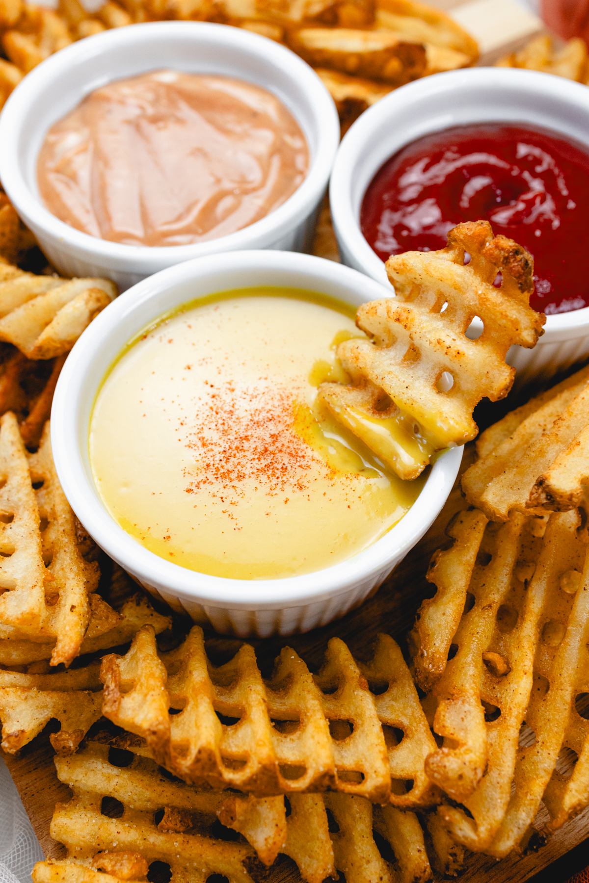 Top view of honey mustard dipping sauce in a small ramekin, next to two other dips, surrounded by waffle fries.