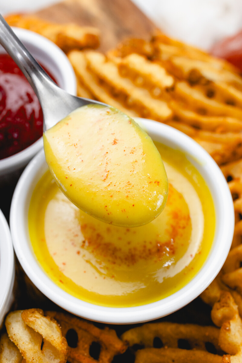 Close up of honey mustard dipping sauce in a ramekin with a spoon in it.