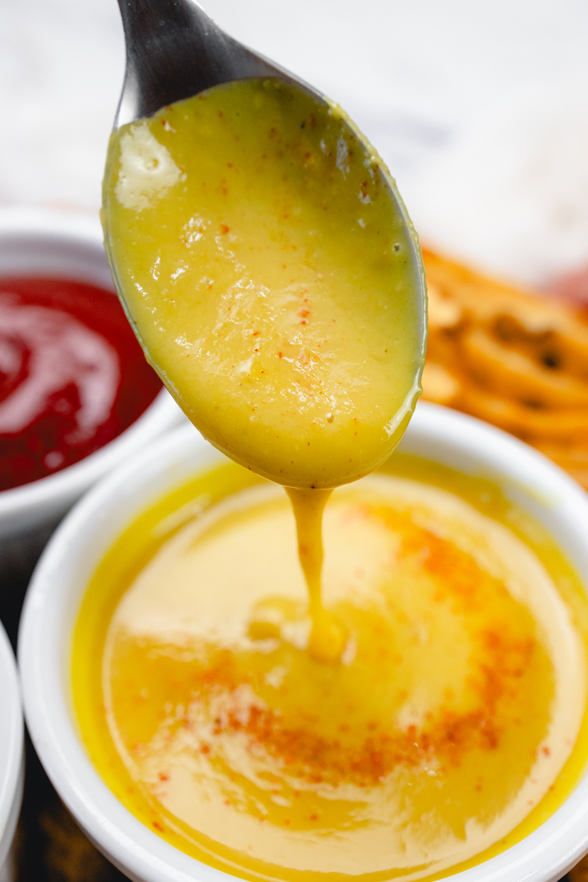 Close up of honey mustard dipping sauce in a ramekin with a spoon in it.
