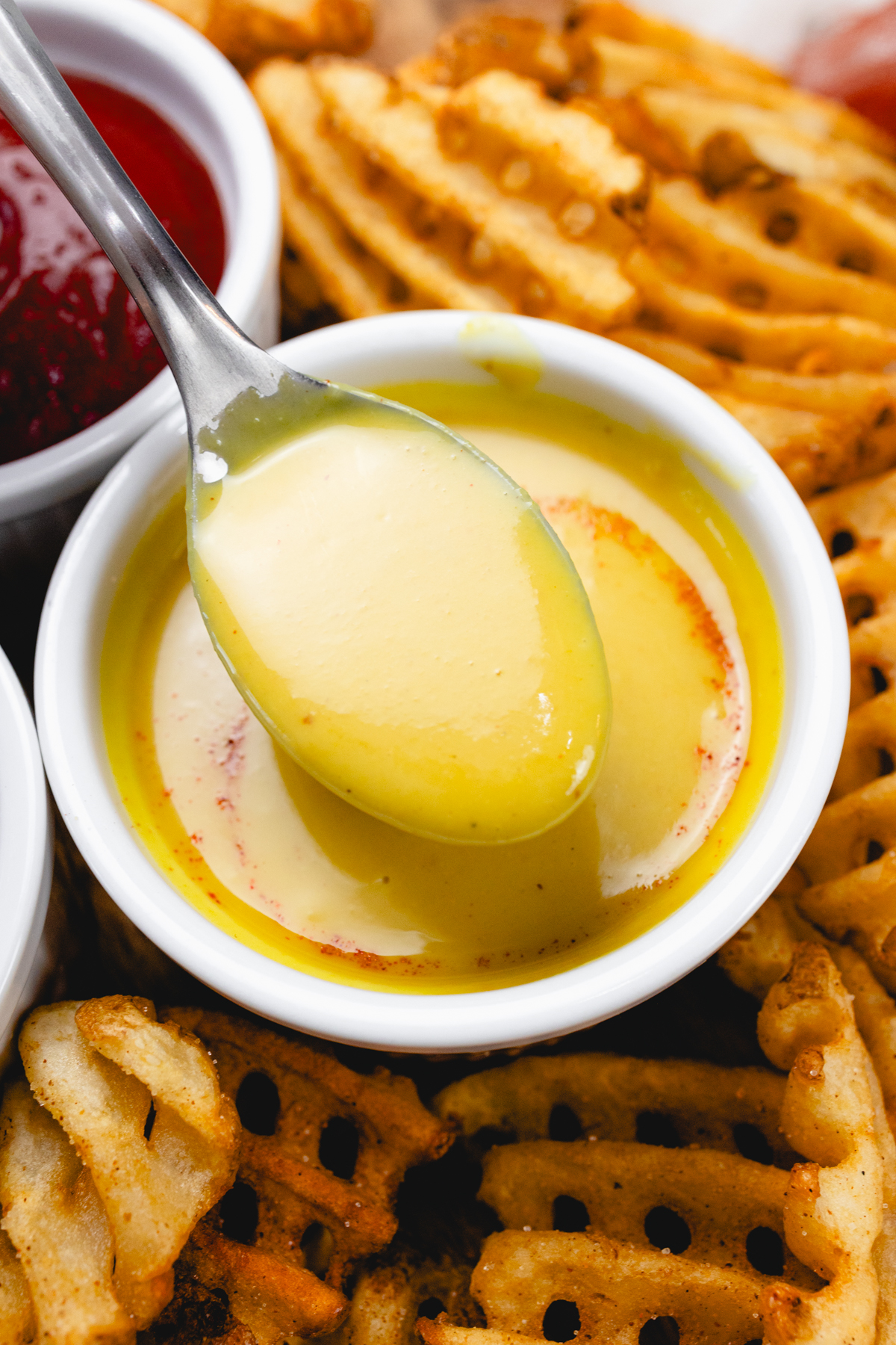 Close up of honey mustard dipping sauce in a ramekin with a spoon in it.