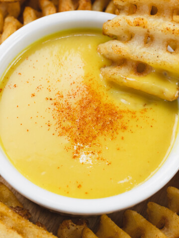 Close up of honey mustard dipping sauce in a ramekin with a waffle fry being dipped into it.