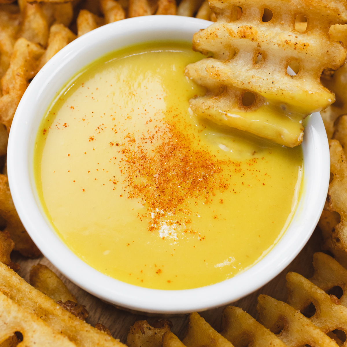 Close up of honey mustard dipping sauce in a ramekin with a waffle fry being dipped into it.