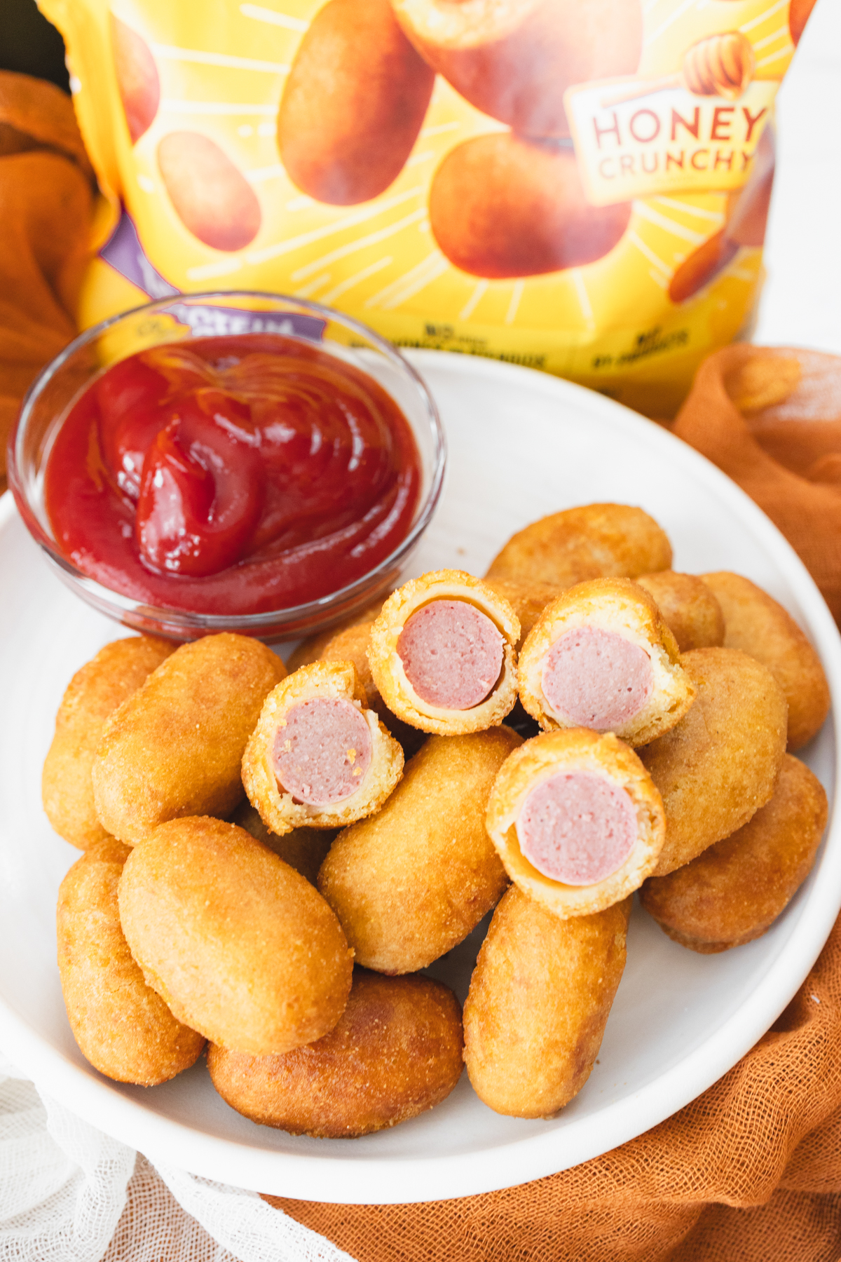 Close view of cooked mini corn dogs on a white plate that has a small dipping bowl of ketchup on it.