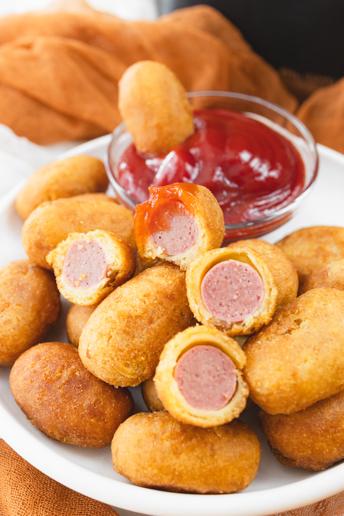 Close view of cooked mini corn dogs on a white plate that has a small dipping bowl of ketchup on it.