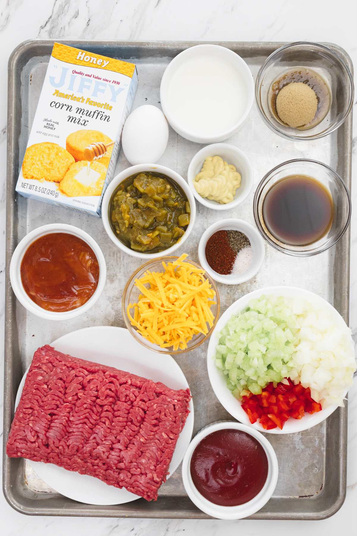 Top view of ingredients needed to make Sloppy Joes Cornbread Casserole recipe in small bowls on a baking tray.