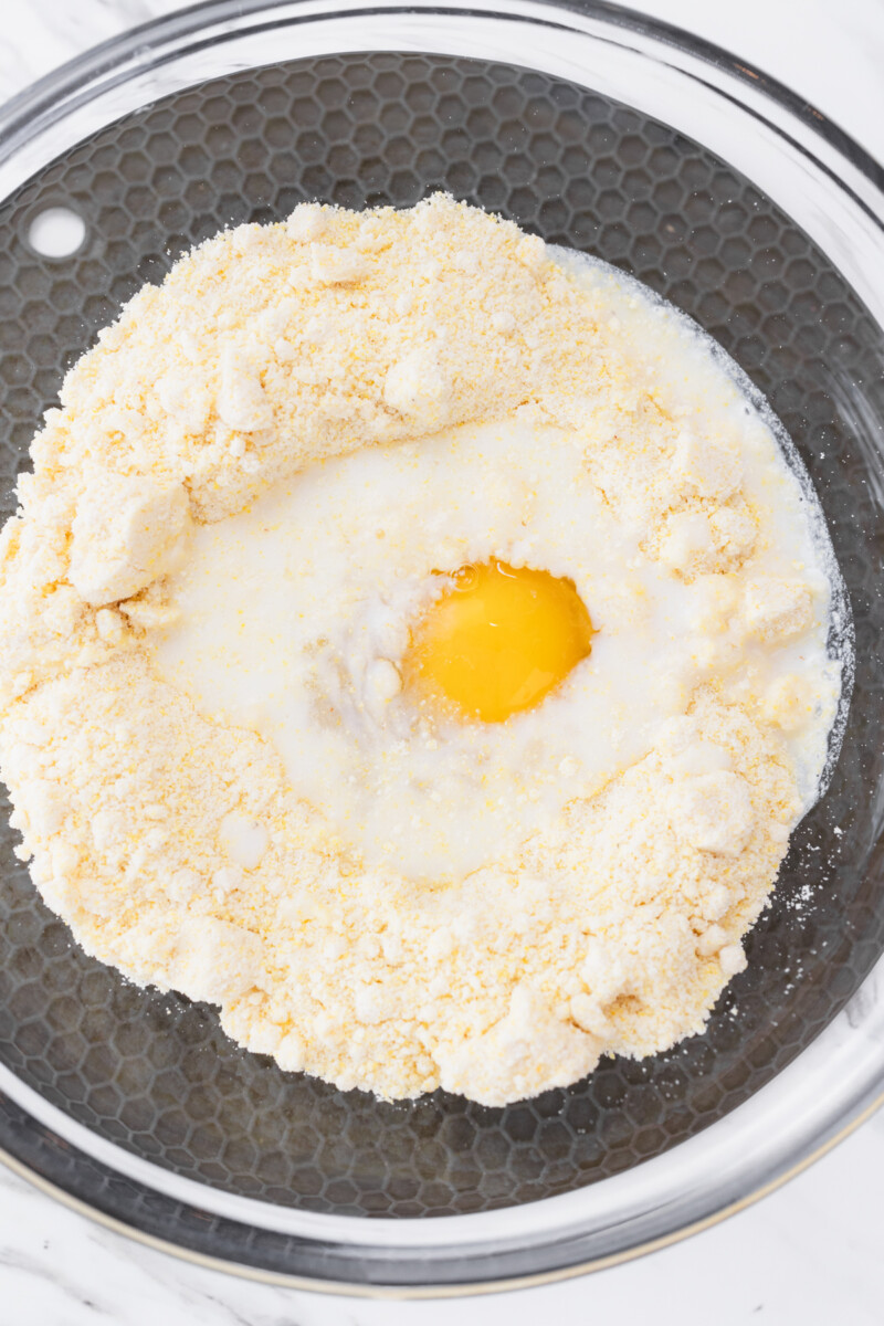 Close up of the mixing bowl containing the cornbread mixture, with milk and an egg on top.