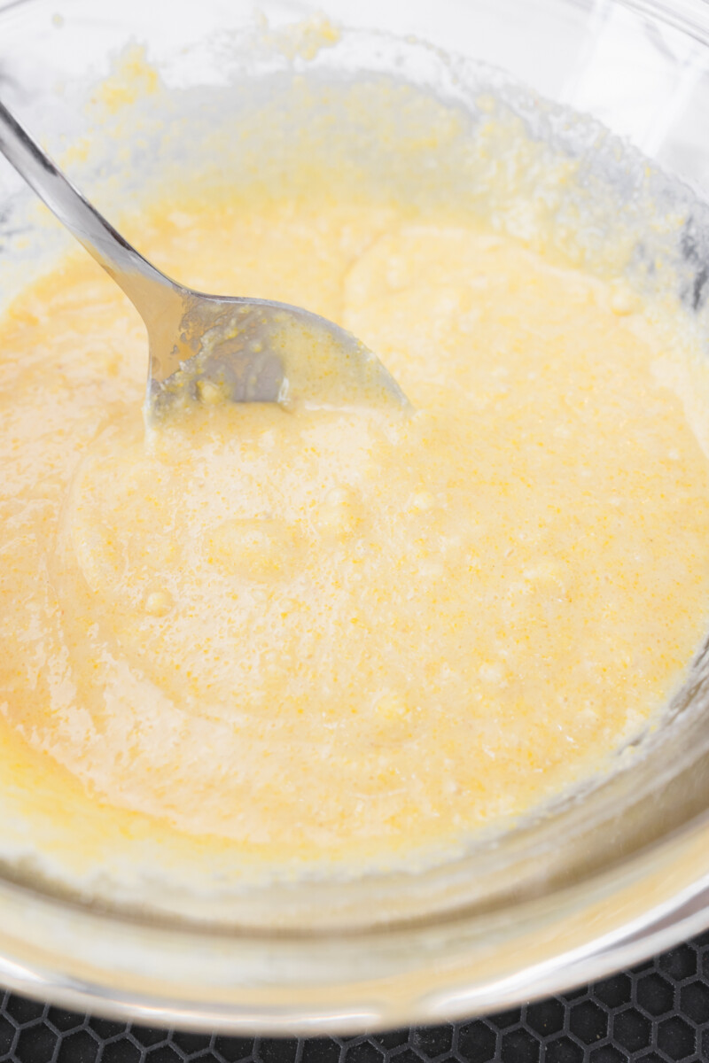 Close up view of the cornbread mixture being combined in the mixing bowl using a spoon.