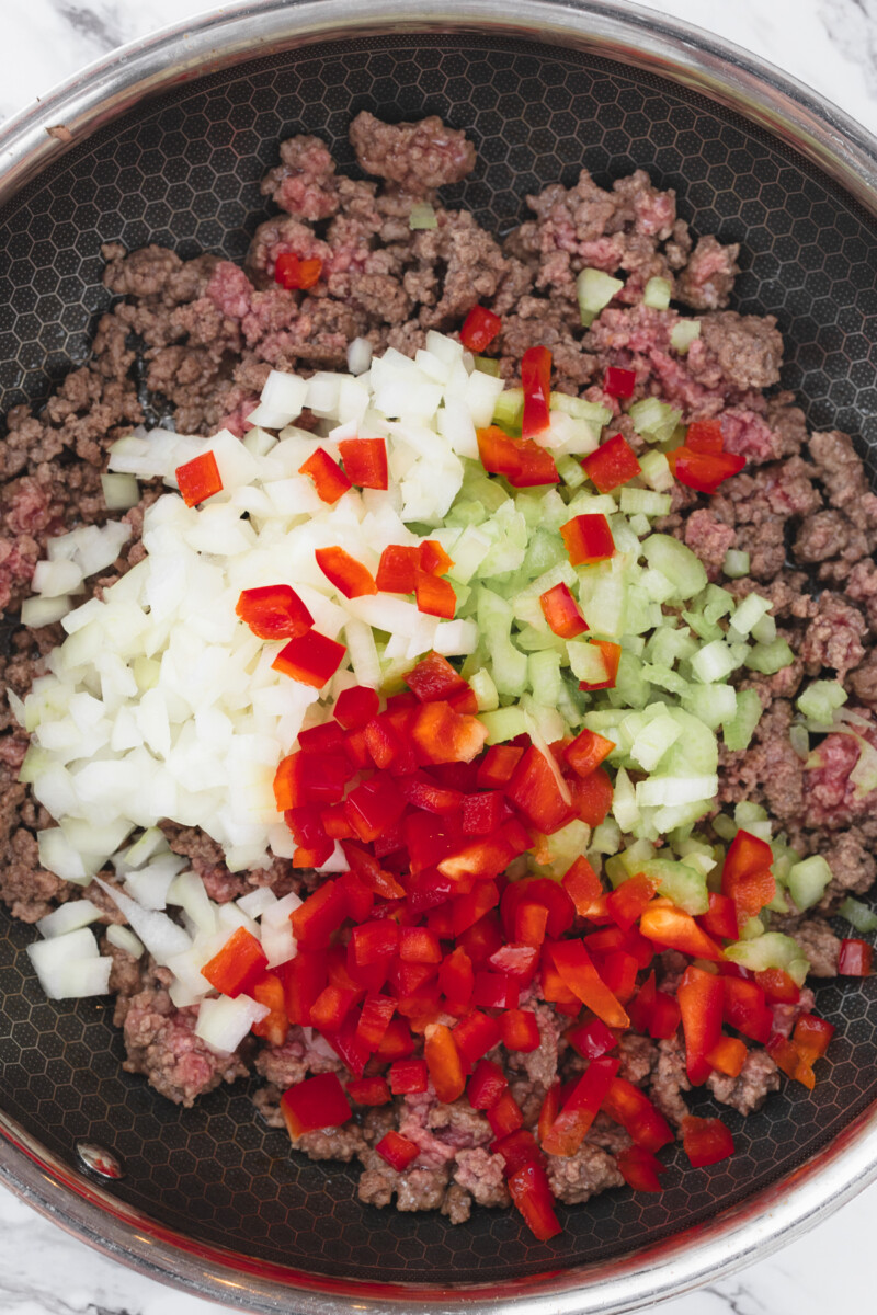 Top view of gorund beef in a pan with diced vegetables on top.