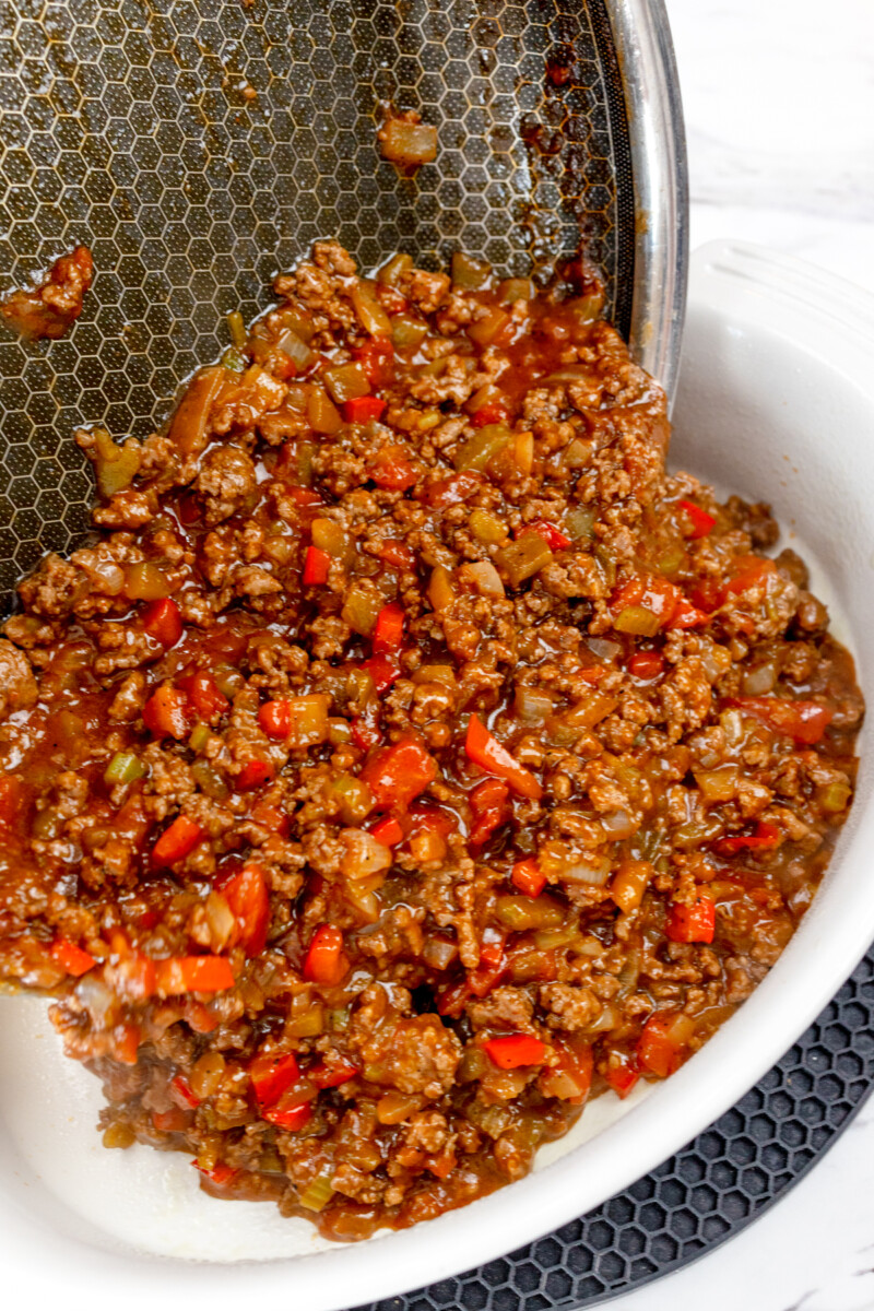Close up view of sloppy joe mixture being poured into a casserole dish.
