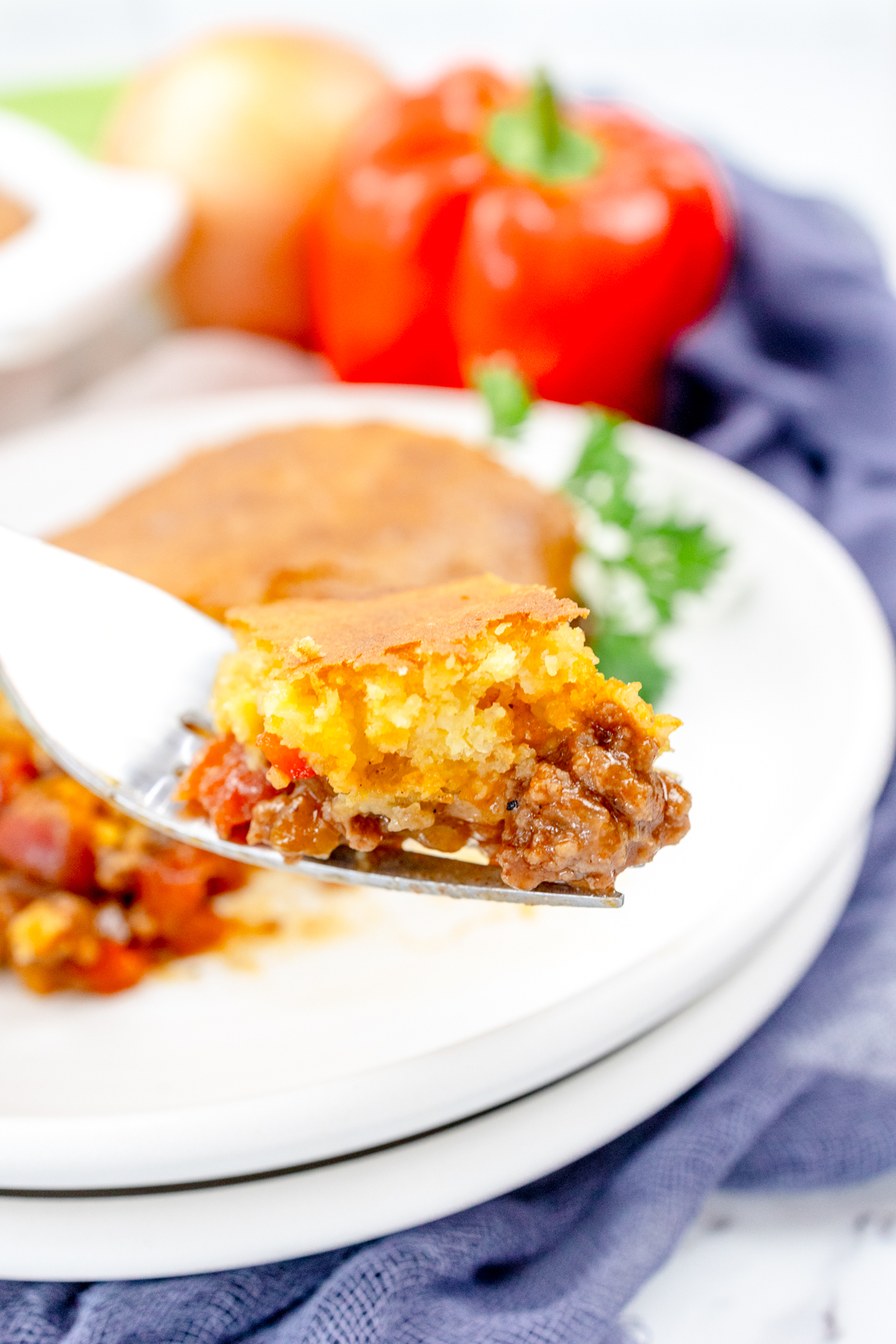 Close up view of a fork with sloppy joe casserole on it, with a white plate in the background that has more sloppy joe casserole on it.