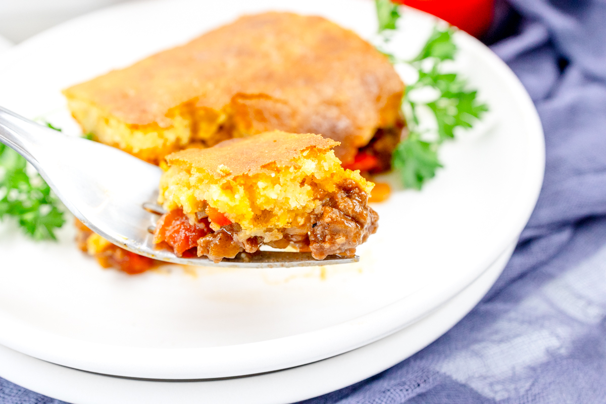 Close up view of a fork with sloppy joe casserole on it, with a white plate in the background that has more sloppy joe casserole on it.