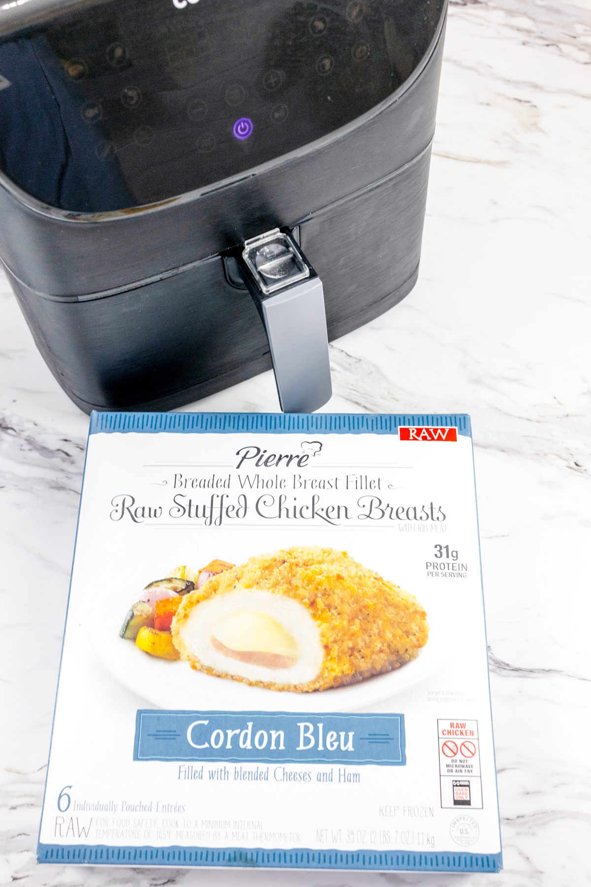 Angled view of a package of frozen Chicken Cordon Bleu in front of an air fryer.