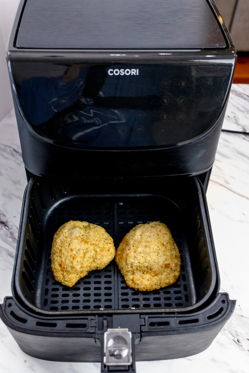 Angled view of two uncooked frozen Chicken Cordon Bleu portions in an air fryer basket.