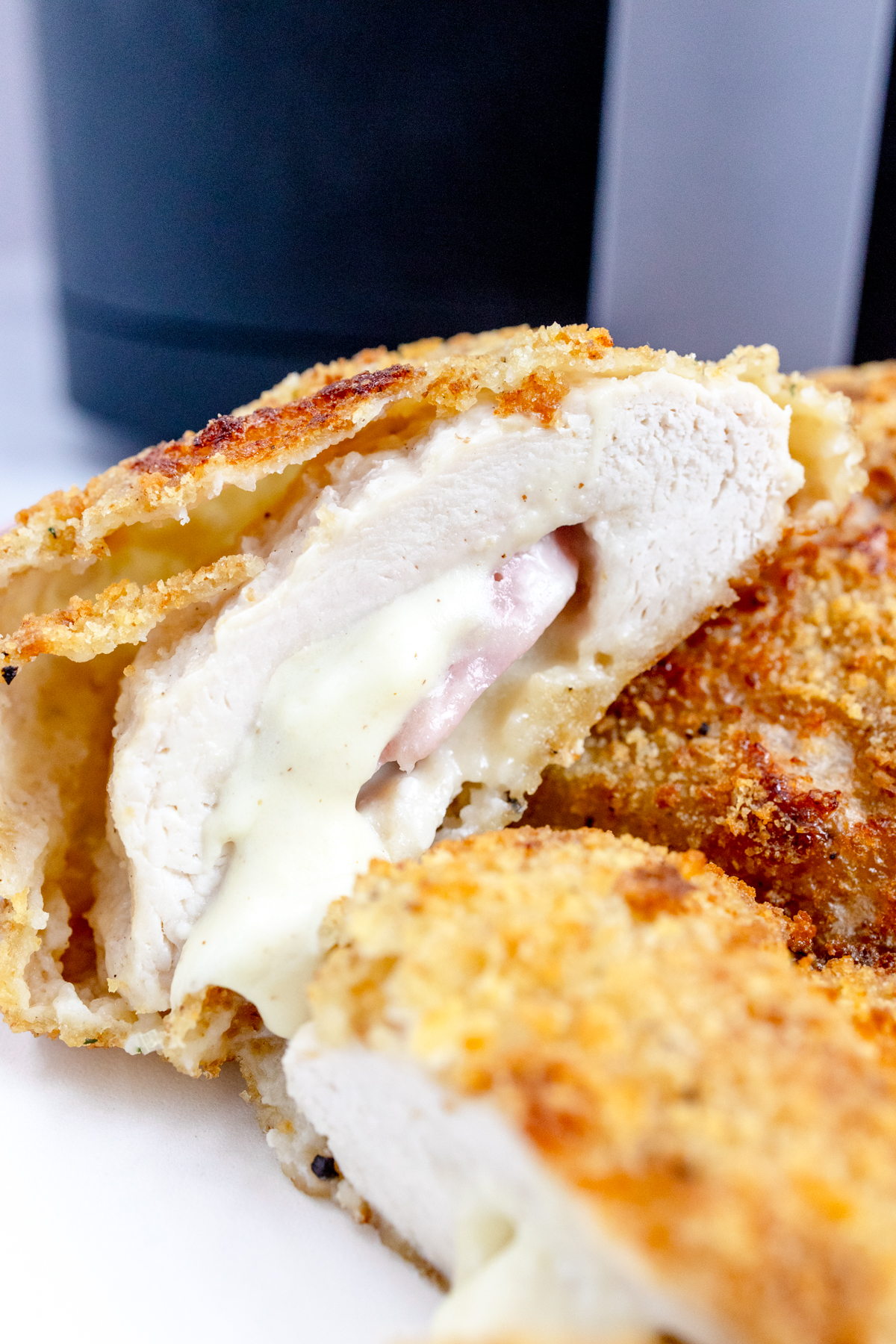 Close up image of Air Fried Chicken Cordon Bleu on a white plate in front of an air fryer.