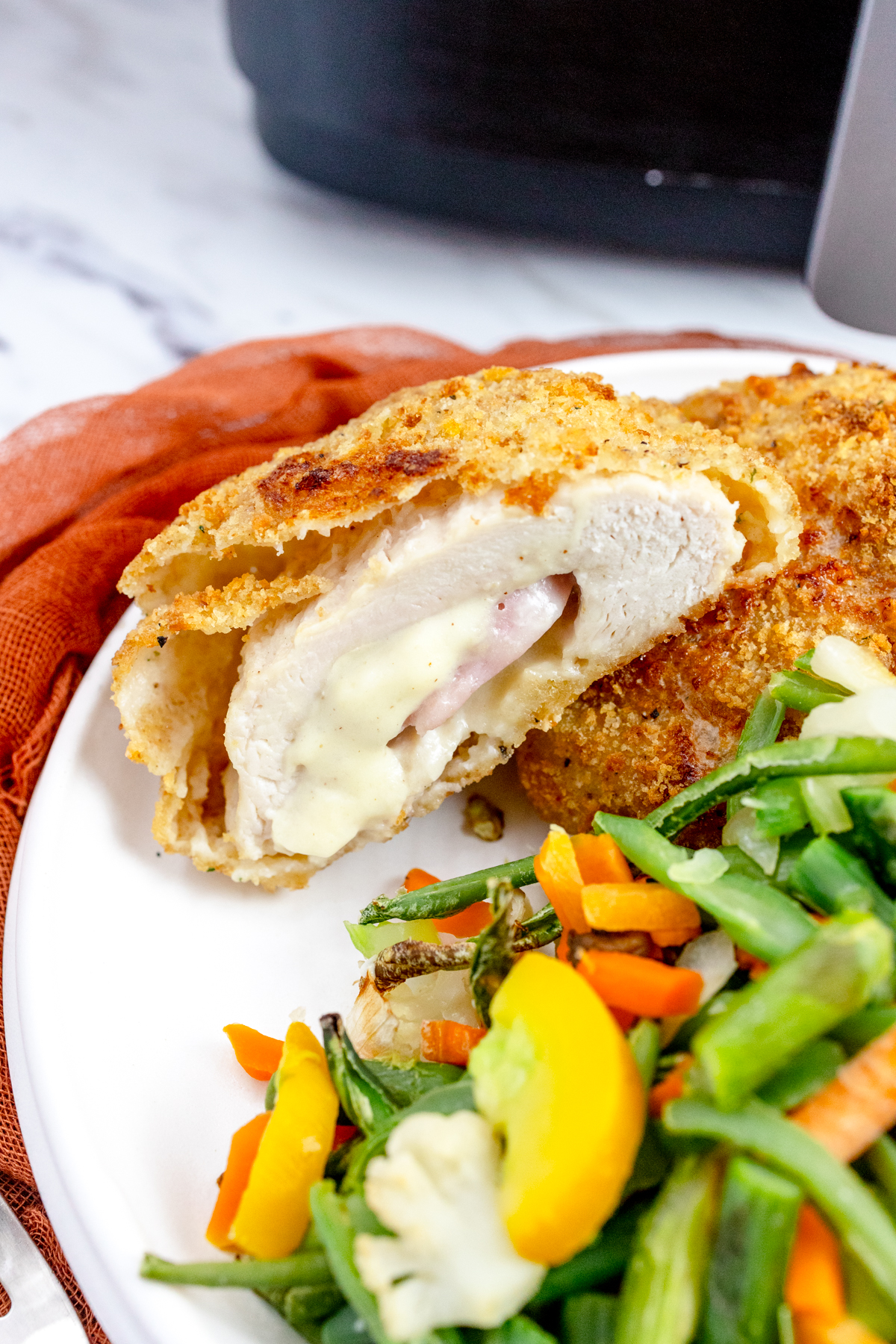 Angled view of Air Fried Chicken Cordon Bleu on a white plate with side vegetables on the side.