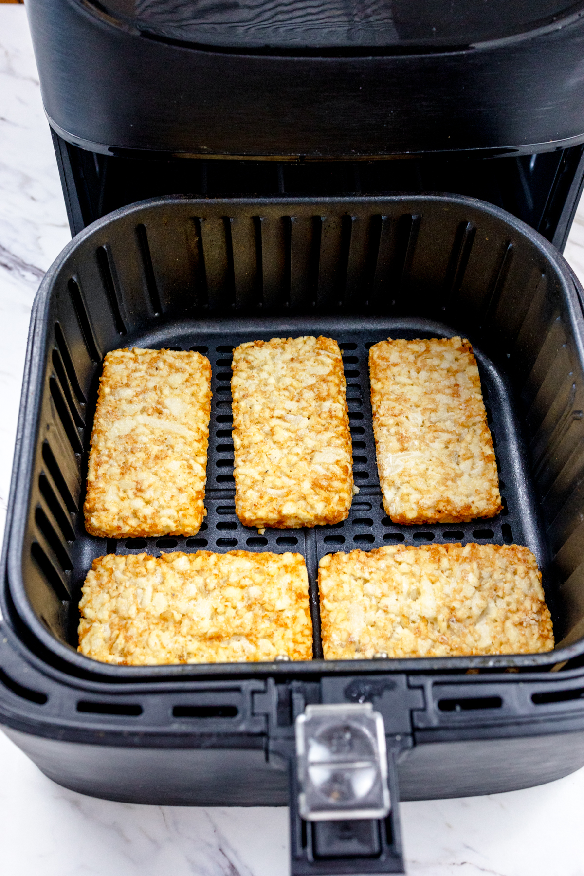 Top view of frozen hash browns in an air fryer basket.
