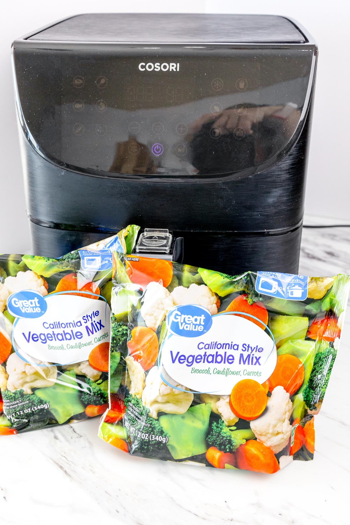 Bags of frozen vegetables in front of an air fryer.