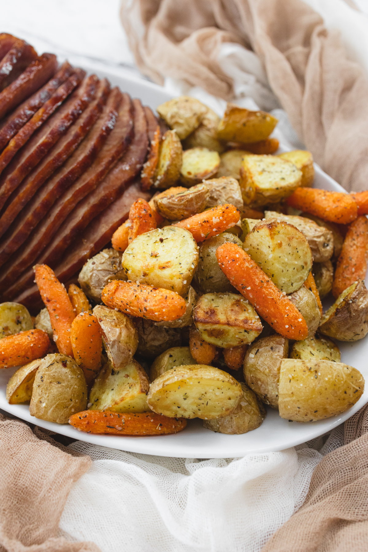 A close up view of carrots and potatoes on a white plate with sliced ham.