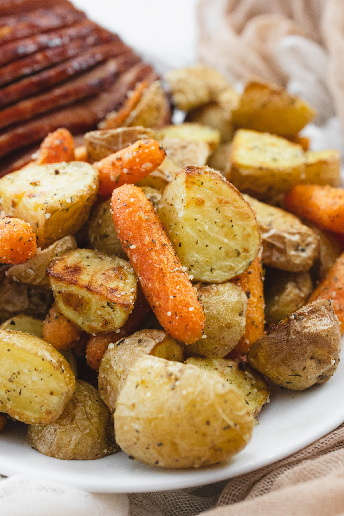 A close up view of carrots and potatoes on a white plate with sliced ham.