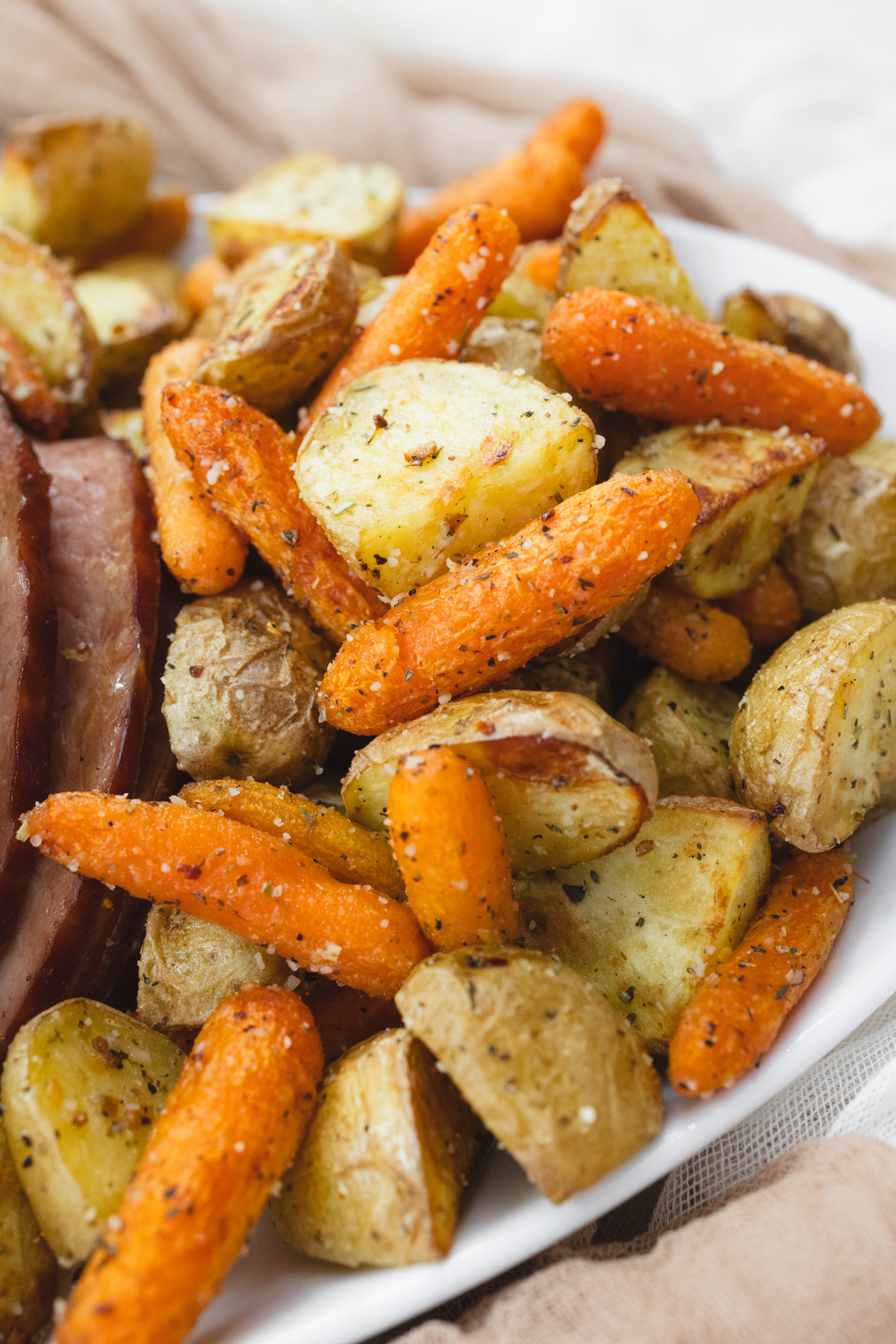 A close up view of carrots and potatoes on a white plate with sliced ham.