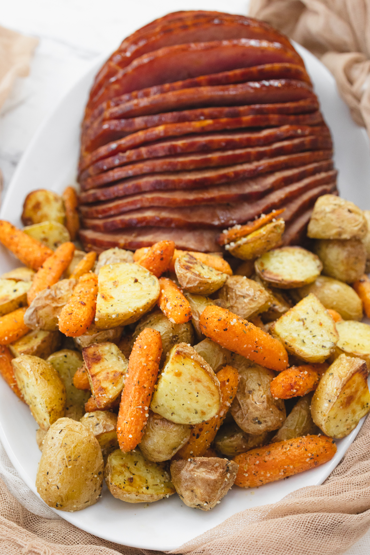 A top view of carrots and potatoes on a white plate with sliced ham.