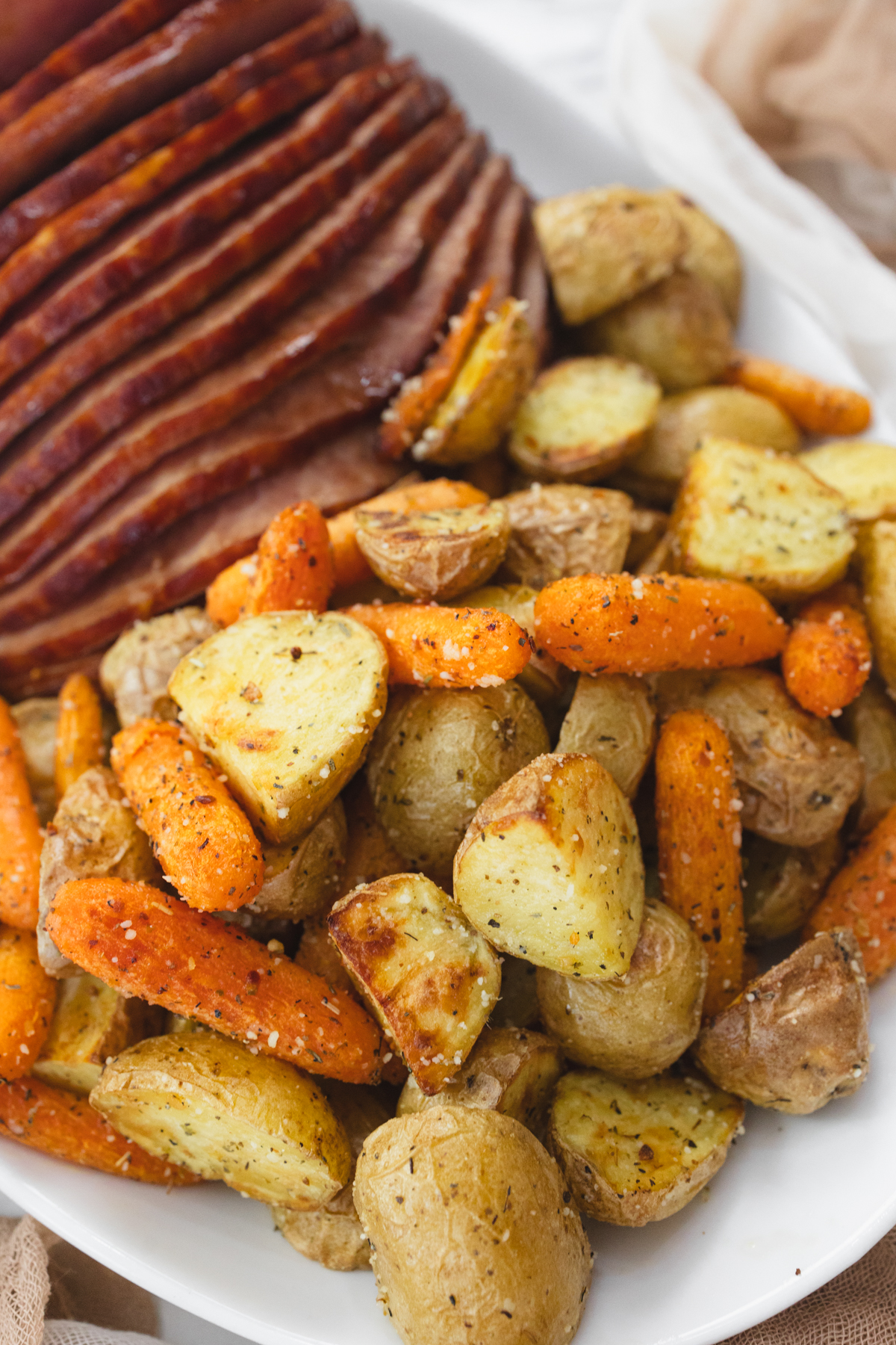 A top view of carrots and potatoes on a white plate with sliced ham.