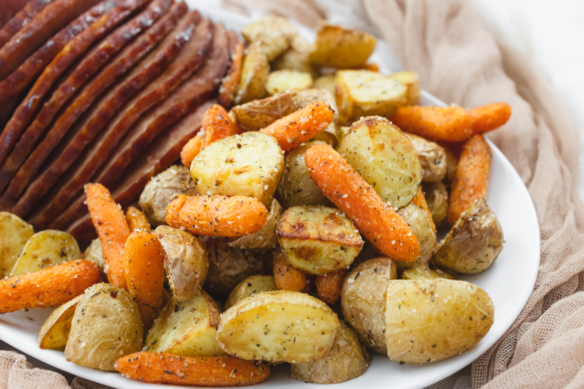 A close up view of carrots and potatoes on a white plate with sliced ham.