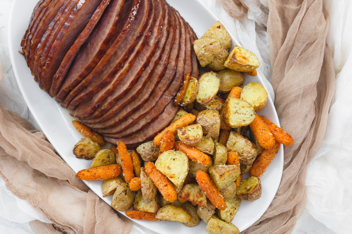 A top view of carrots and potatoes on a white plate with sliced ham.