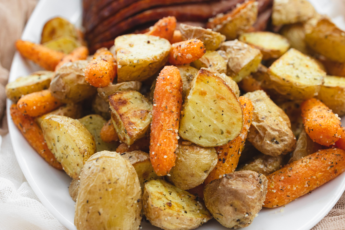 A close up view of carrots and potatoes on a white plate with sliced ham.