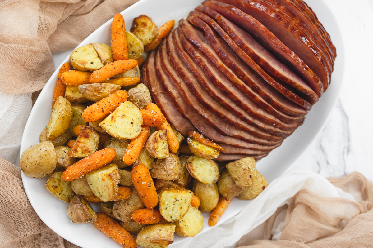 A top view of carrots and potatoes on a white plate with sliced ham.