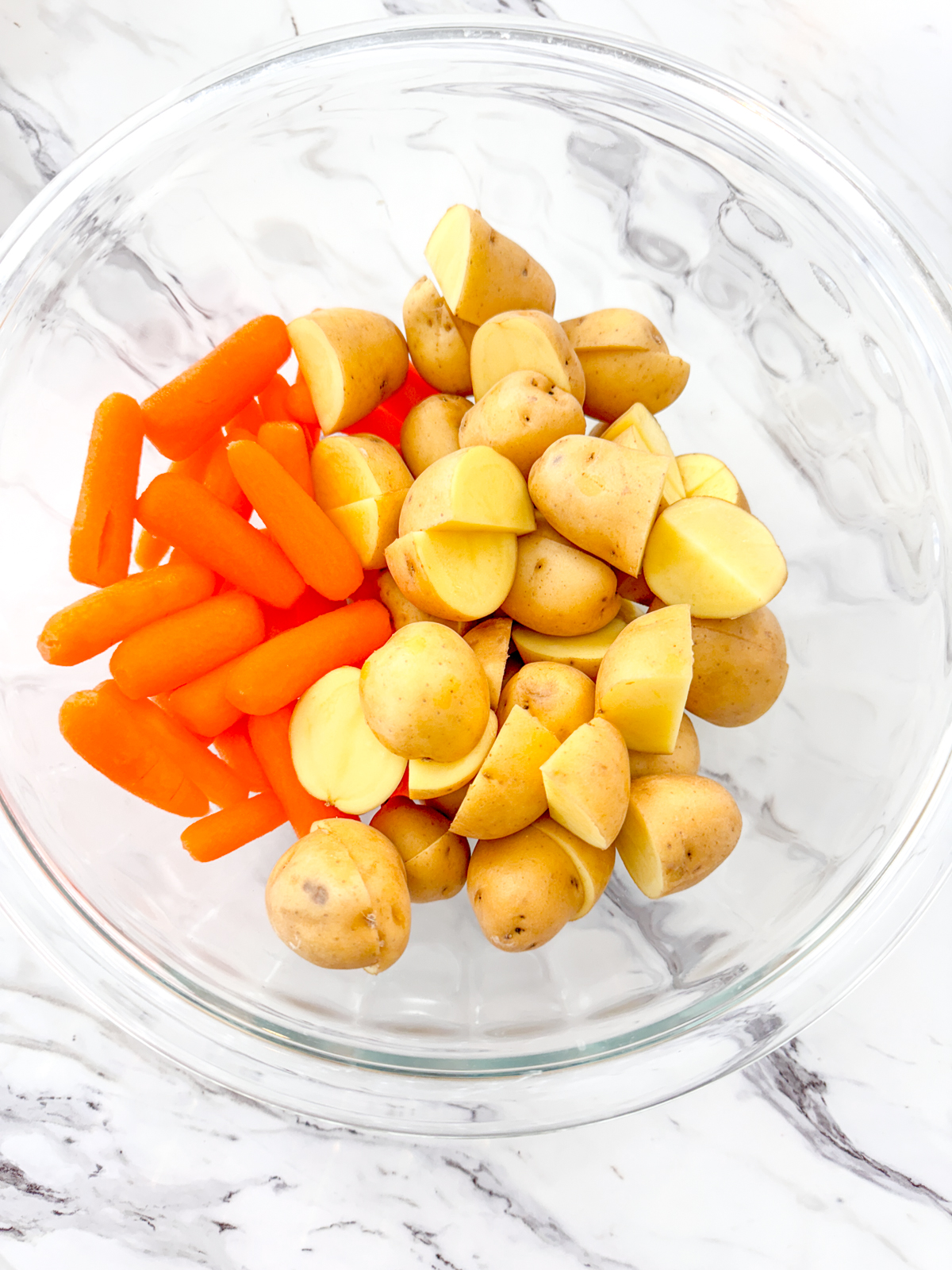 A top view of carrots and potatoes in a glass bowl.